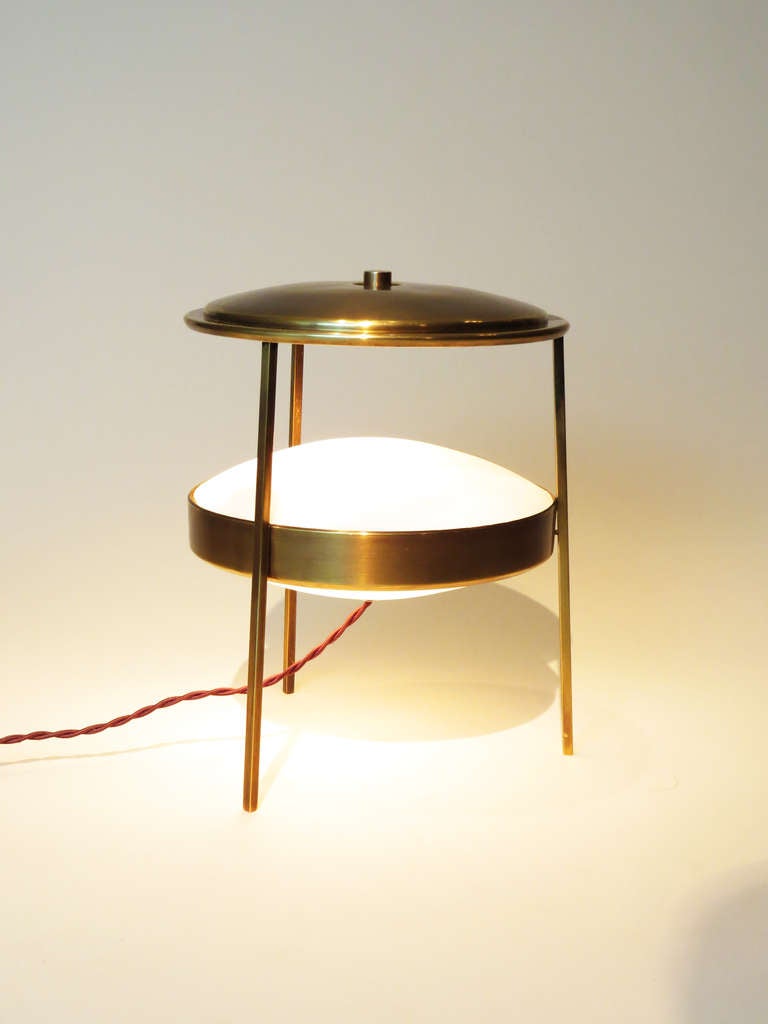 Small, but stunning table lamp made of brass and frosted glass. Has three legs that hold up the light and the top lid further up.