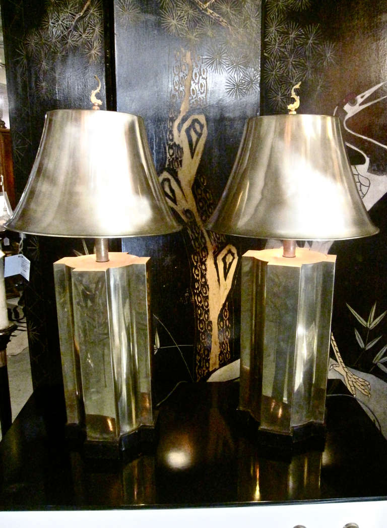 This is an outstanding pair of solid brass lamps that dates to the late 1970's. The lamps are in a style reminiscent of James Mont. In addition to the brass cross shaped column base, the unique heavy shades are also solid brass. The cast brass