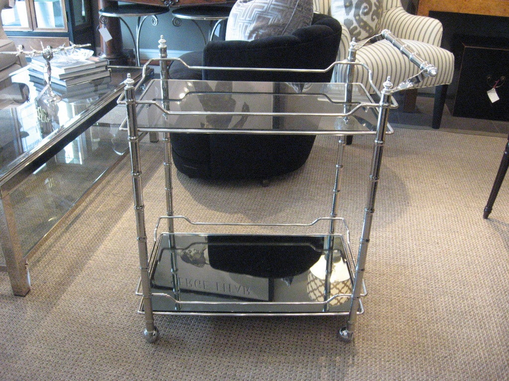 Stunning vintage polished nickel bar/tea cart featuring faux bamboo handle and legs and tinted glass upper shelf and smoked mirror bottom shelf.