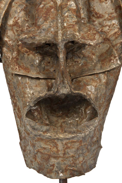 Large sculptural metal mask mounted on an iron stand