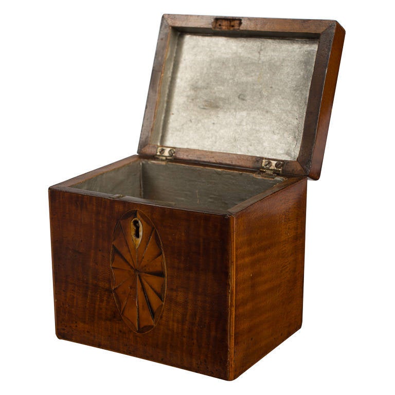 English tea caddy made of inlaid mahogany from the Gerogian-era, featuring inlaid georgian motif on the top surrounding a metal pull ring. Front with similar inlay and a brass keyhole escutcheon. Interior with zinc lining. c.1790