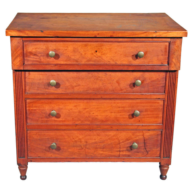 Probably Mid Atlantic, circa 1820.  Having an over-hanging top drawer above three drawers flanked by reeded pilasters supported by turned feet.

17 1/2