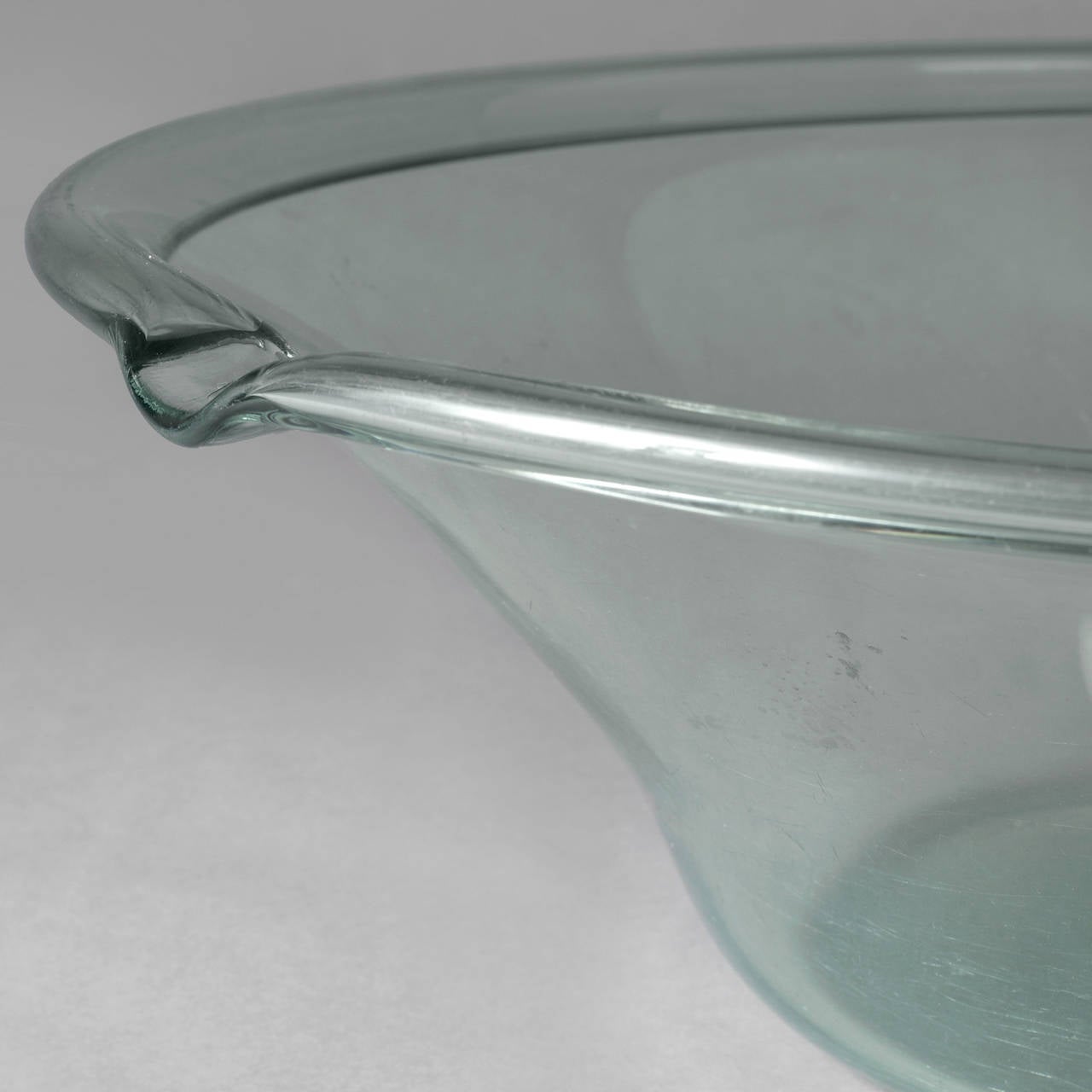 Probably French, early-mid-19th c.
Blown glass, aqua-marine color.
Excellent condition,customary wear to the base.
Commonly mistaken for American milk pans, this rare large scale example has a folded rim, pouring spout, and a polished pontil, and