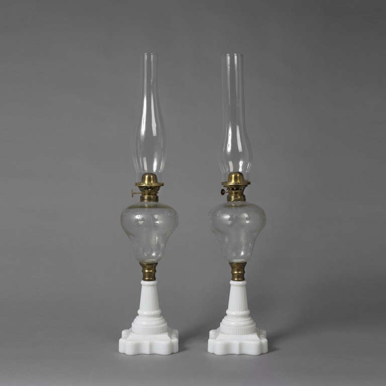 American, late 19th c.
Blown and pressed glass
Excellent condition
The lamps with colorless fonts are ornamented with cut and wheel engraved spreading eagles, stars and fruiting vines above pressed milk glass bases, both with brass kerosene