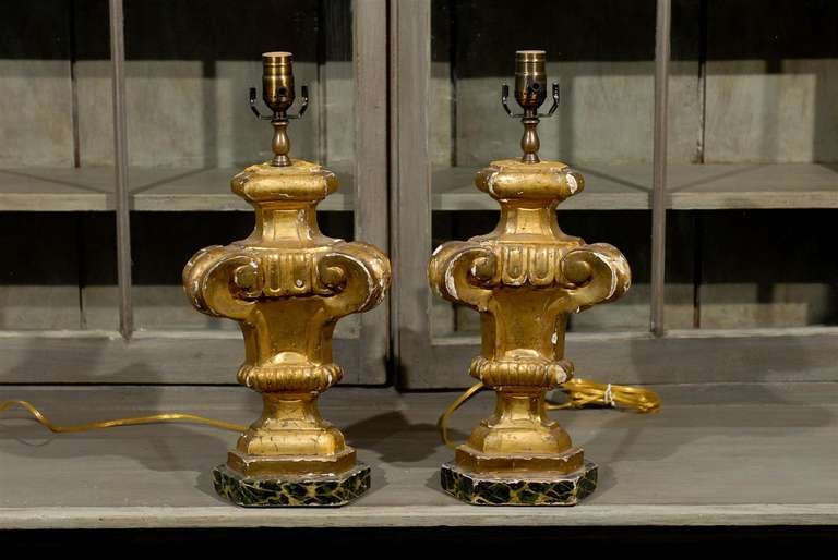 A pair of European, 19th century gilded table lamps standing on faux-marble bases. The front of the table lamps are gilded while the other sides are painted.

These gilded wooden lamps have been rewired for the US market.
