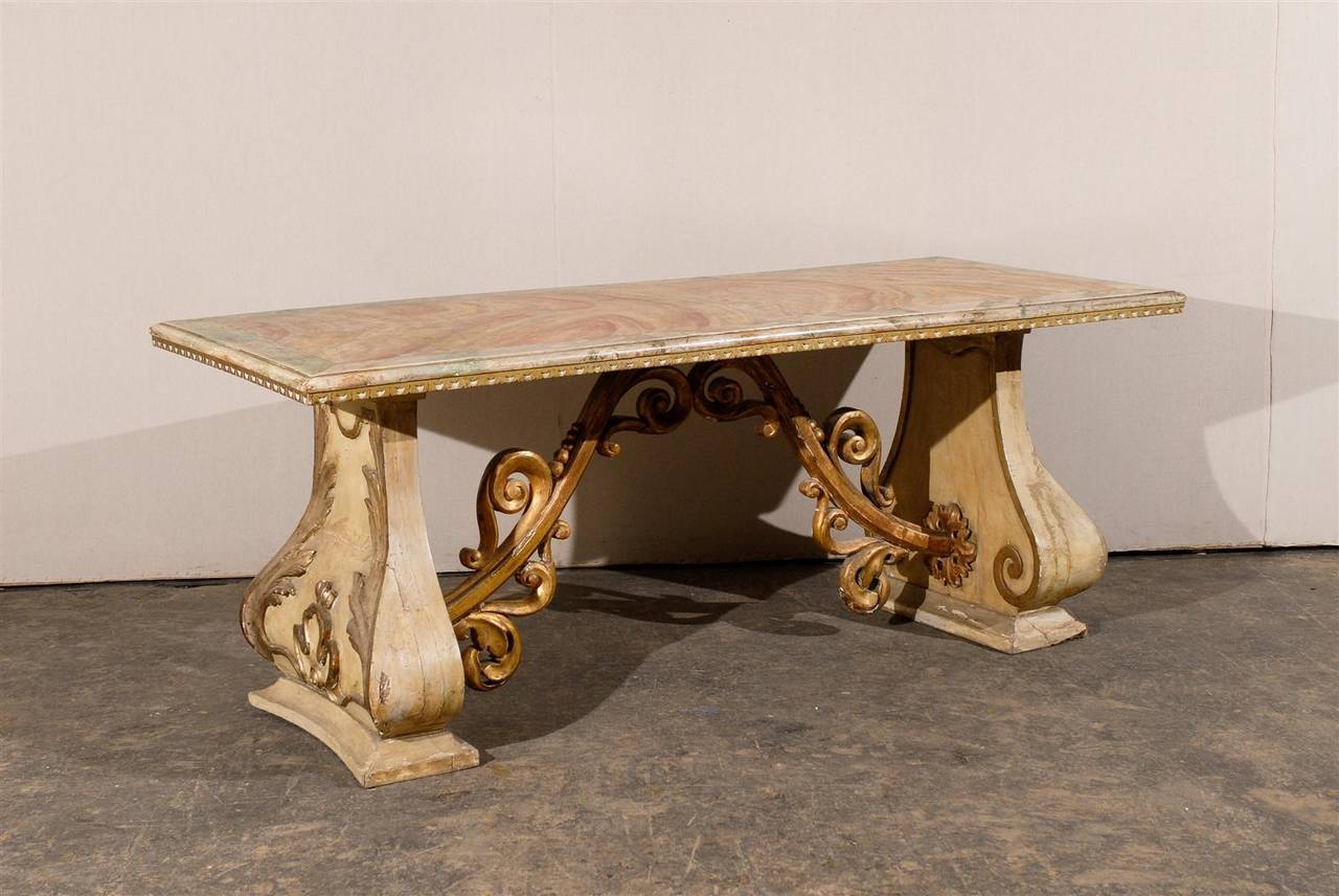 This Italian 19th century console table has an incredible Baroque presence.

From its richly decorated carved legs emerges its gilded wood stretcher whose volutes come and meet at the center. Its faux marble top, wrapped in a thin molding, crowns