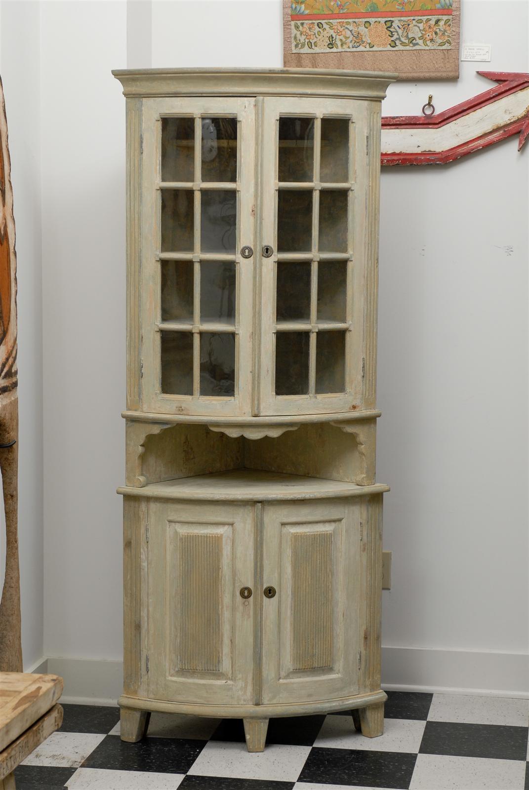 This delightful late 18th-early 19th century Swedish corner cabinet is made of a convex top part with glass doors and multiple inner shelves. It rests on the lower part made of two paneled doors opening on a space divided by a shelf. 
The piece is