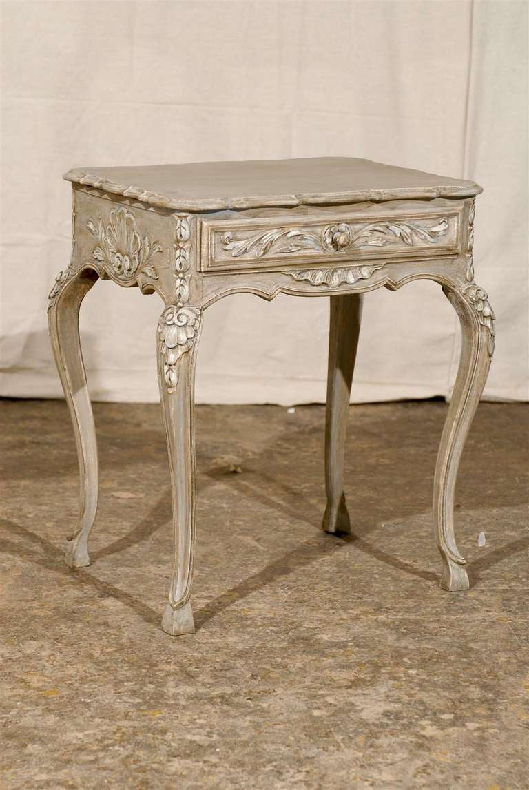 A small carved and painted wood French side table with single drawer. This French early 20th century side table features a richly carved single drawer with foliage motifs as well as shell motifs on the sides. The table is raised on cabriole legs