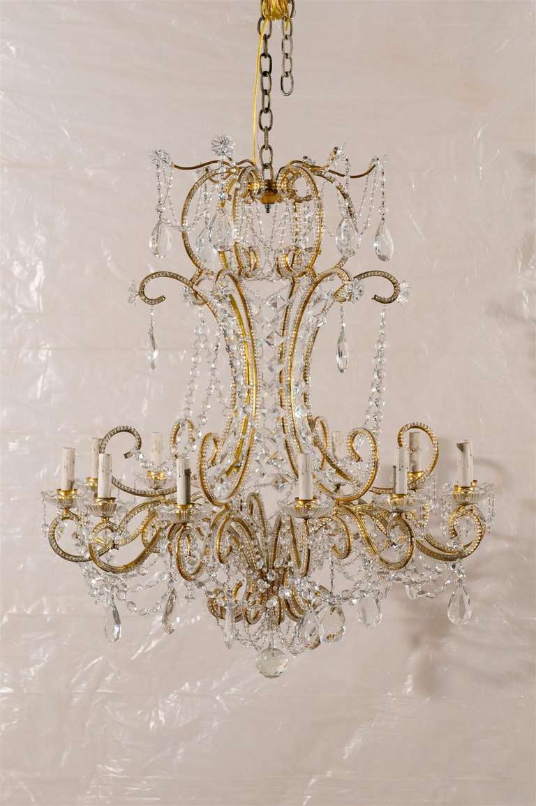 An Italian vintage twelve-light crystal chandelier. This exquisite Italian mid-20th century crystal chandelier features a gilded metal armature made of an abundance of c-scrolls to which scrolled arms are attached. The whole armature is decorated