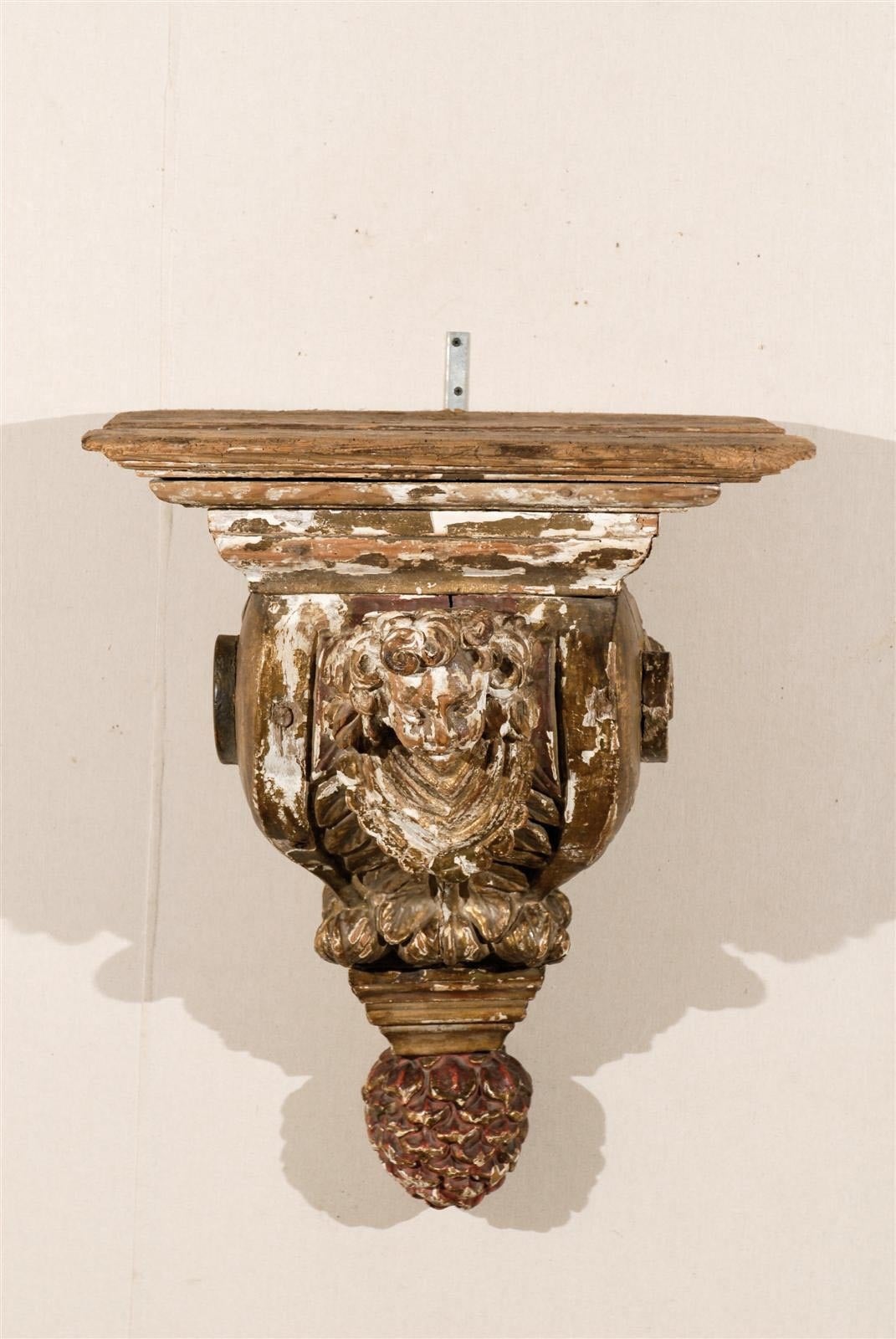 An 18th century architectural gilded and painted wood bracket with carved angel and pine cone finial.