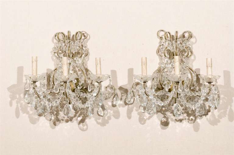 A pair of Italian vintage three-light crystal sconces. This pair of Italian crystal sconces from the mid-20th century features a variety of faceted crystals ornately decorating the scrolled and gilded metal armature and arms. Strands of crystals