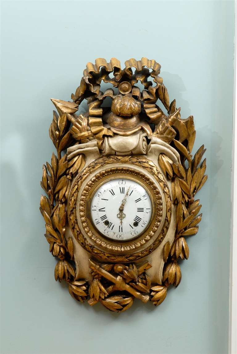Painted and gilded French wall clock, from the late 19th / early 20th century. 

This stunning clock is crafted with a flavor of antiquity, featuring an arrow, an ax, a quiver, a feathered helmet and a pair of flutes. In addition, the clock is