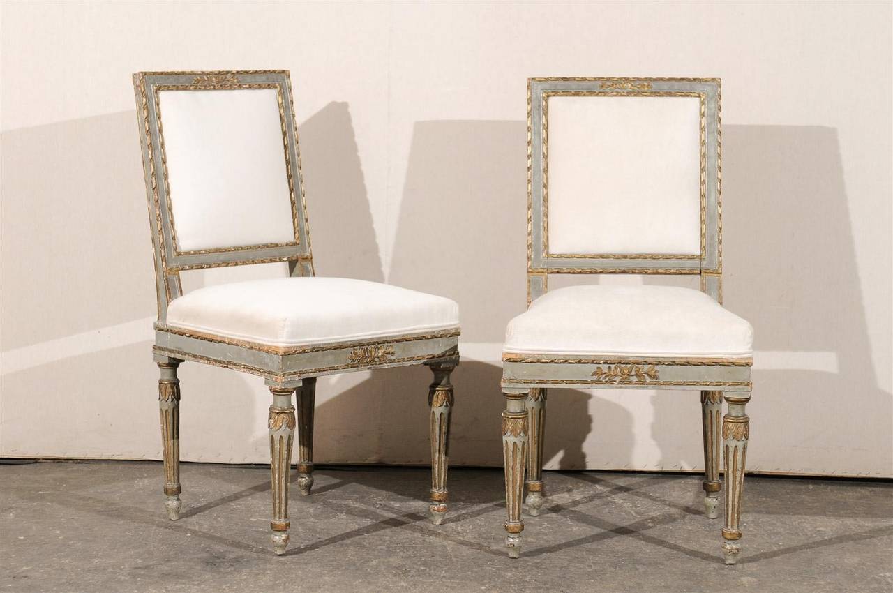 A set of four 18th century Italian painted and gilded upholstered wooden side chairs with slanted backs, foliage carving on the skirt and fluted legs.