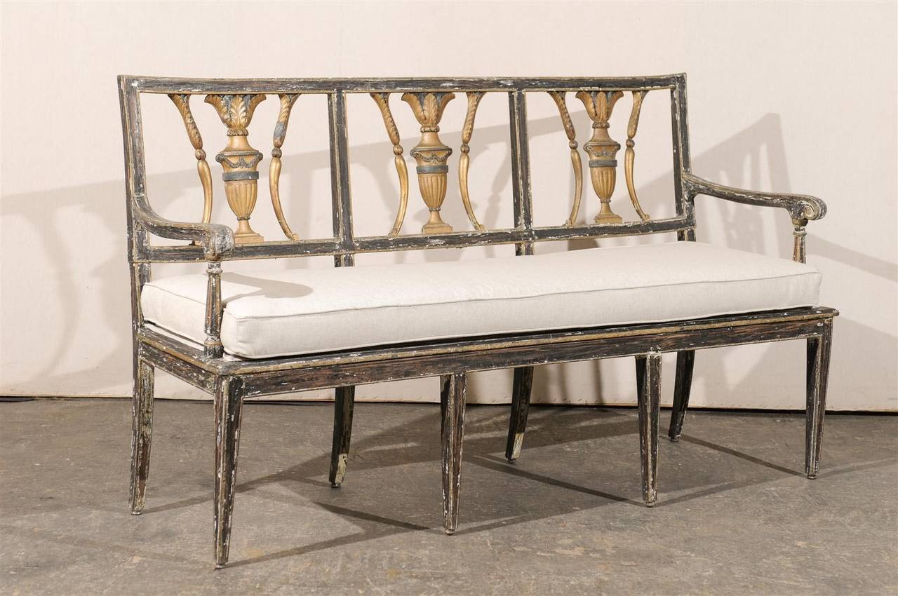 An Italian early 19th century painted and gilded wooden bench or sofa with carved and gilded splats, custom cushion in Belgian linen and tapered feet.