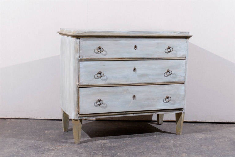 A Swedish mid-19th century Gustavian Style three-drawer chest with raised top and angled, tapered feet. The general color tone of this Swedish chest is made of blue and green. The trim is brown.