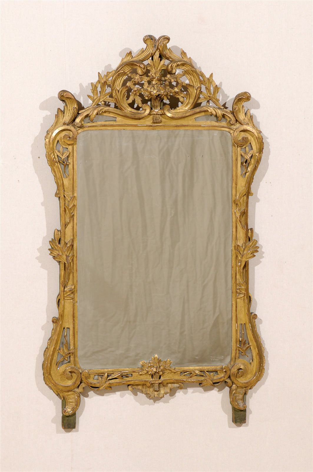 A French mid-19th century richly carved gilded wood mirror with C-scroll patterns. The delicately carved crown with its laurel leaves and flower bouquet motifs echoes the lower part, ornate with a discreet bouquet of flowers as well.