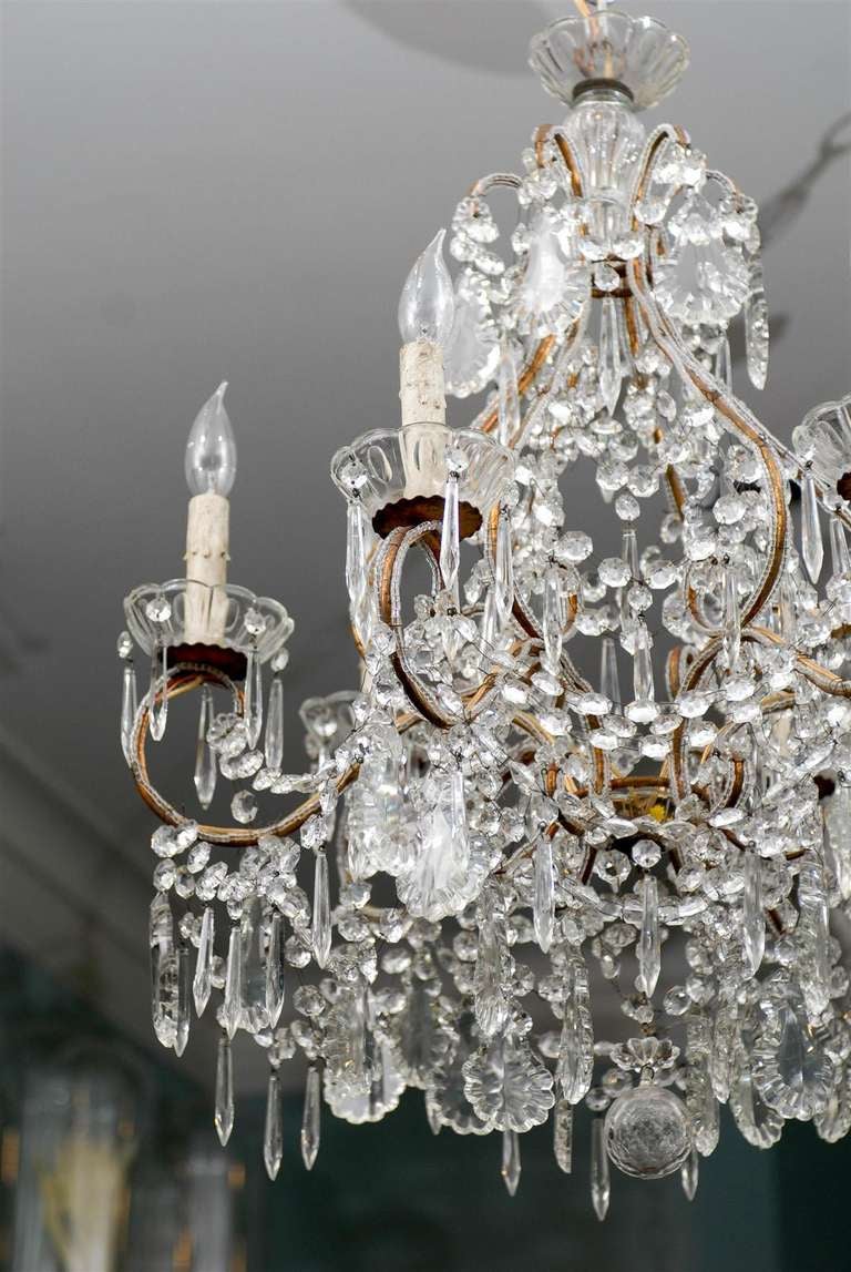 An Italian six-light crystal chandelier with round shaped crystal finial. This Italian crystal chandelier from the mid 20th century features a gilt metal armature made of various scrolls, as well as scrolled arms supporting their glass bobèches and