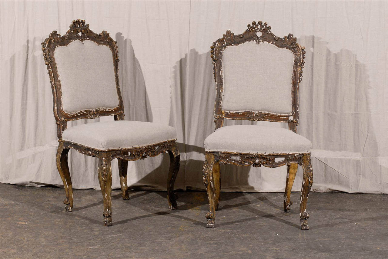 A pair of richly carved Italian, 18th century Venetian style upholstered chairs with slanted backs.

The chairs Stand on four cabriole legs and its skirt is delicately pierced. The crest and ears are nicely carved as well with scrolls. The chairs