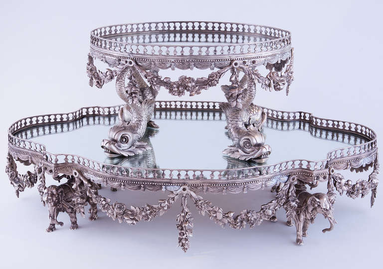 Each graduated tier with pierced galleried edge, the top tier raised on the tails of four stylized dolphins, the bottom tier raised on the backs of four elephants surmounted by urns, overall hung with floral swags.