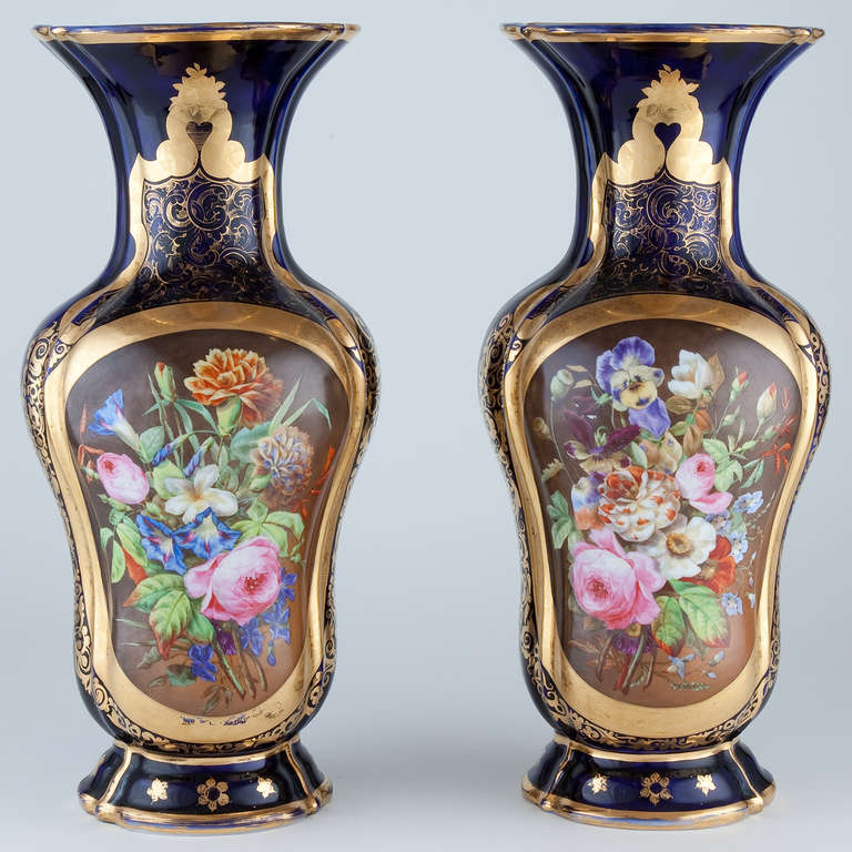 An elegant pair of cobalt blue-ground parcel-gilded bulbous-shaped vases, the facades finely painted with realistic bouquets of flowers within bronze-ground gilt-edged scrollwork cartouches raised on low scalloped bases. Unmarked, probably English.