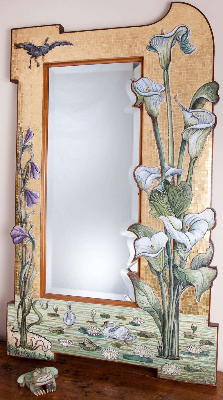 A magnificent period shaped and beveled glass mirror mounted in an asymmetrical wooden frame designed to follow the line of the bevel. Intricate and skillful micro-mosaic work is employed to depict a pond scene with blooming arum lilies and purple