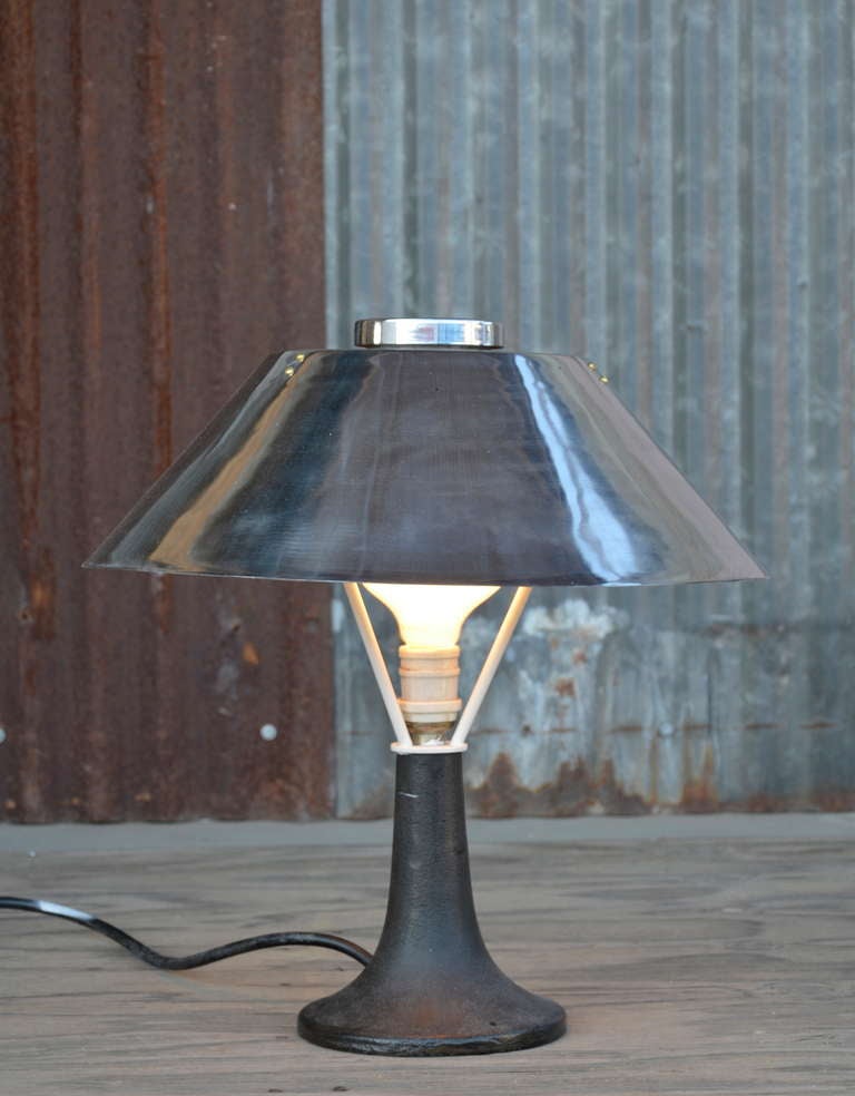 Unusual table lamp constructed of polished steel shade and cast iron base. This lamp was designed for use on sea faring vessels. Excellent man cave accessory.