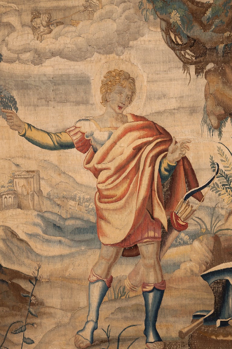 The tapestry depicts Apollo at Vulcan’s forge, the moment when the god Apollo visits Vulcan and tells him that his wife Venus is having an affair with Mars the god of war.  Apollo is shown wearing a red toga turning towards Vulcan who is not seen