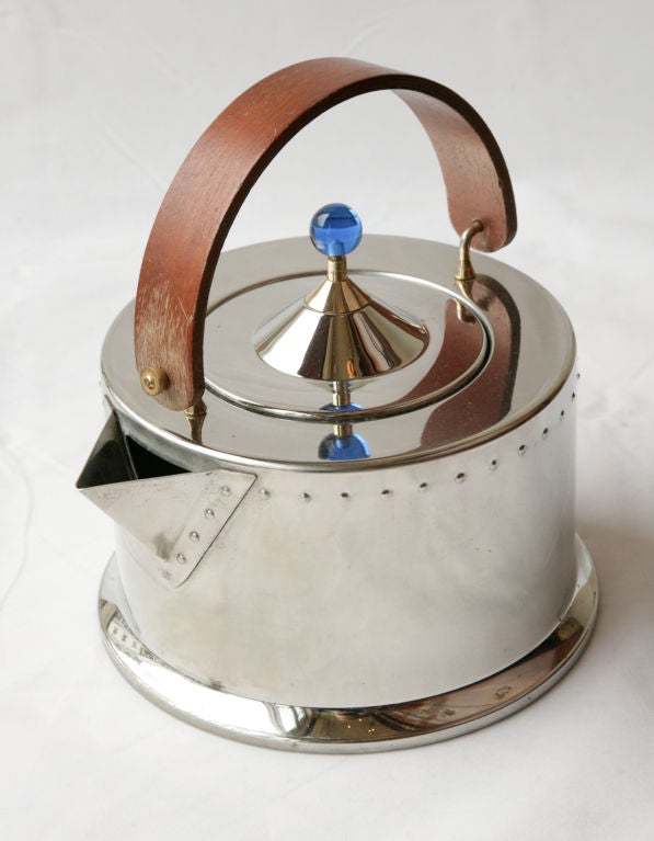 This Bodum Ottoni Kettle was designed by Carsten Jorgensen in the 1980s. It has a round metal body with a flat top and base, a wooden handle, gold plated hinges and a blue acrylic knob on the pointed lid.