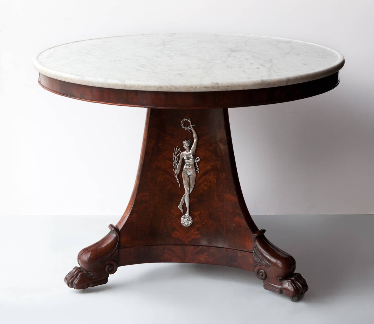 Mahogany and flame mahogany veneer standing on a concave triangular base with paw feet and later castors. White veined carrara marble top on shallow apron. Incised bronze silver plated figures holding laurel wreaths standing on balls decorated with