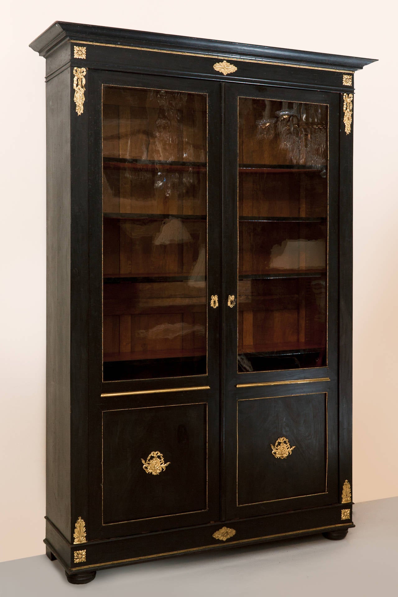 Oak and pine with two glazed doors retaining the original glass. With five pine shelves with ebonised fronts. Gilt bronze decoration including beading around the glass.