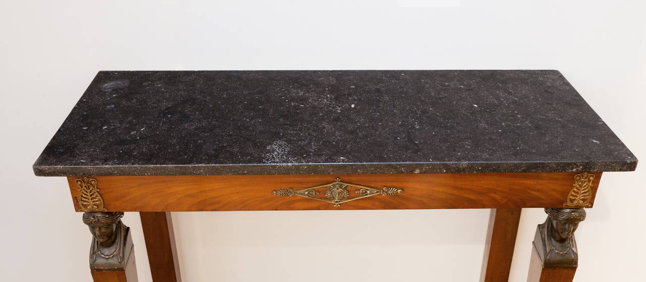 Black fossil marble top, slightly polished, with carved female figures after the antique ebonized to imitate bronze.