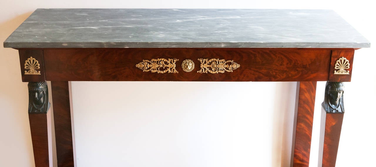 Mahogany with a 'Gris Turquin' marble top. The front tapered legs with patinated bronze heads after the antique terminating in patinated bronze bases, standing on a mahogany plinth. With one wide drawer. Incised gilt bronze mounts to the drawer and