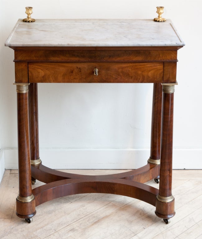 A small French Empire writing table with white marble top with recessed writing area. Gilt bronze mounts and candlesticks.  One central drawer with several separate compartments originally for inkwells etc. There is a slide to reveal two levels in