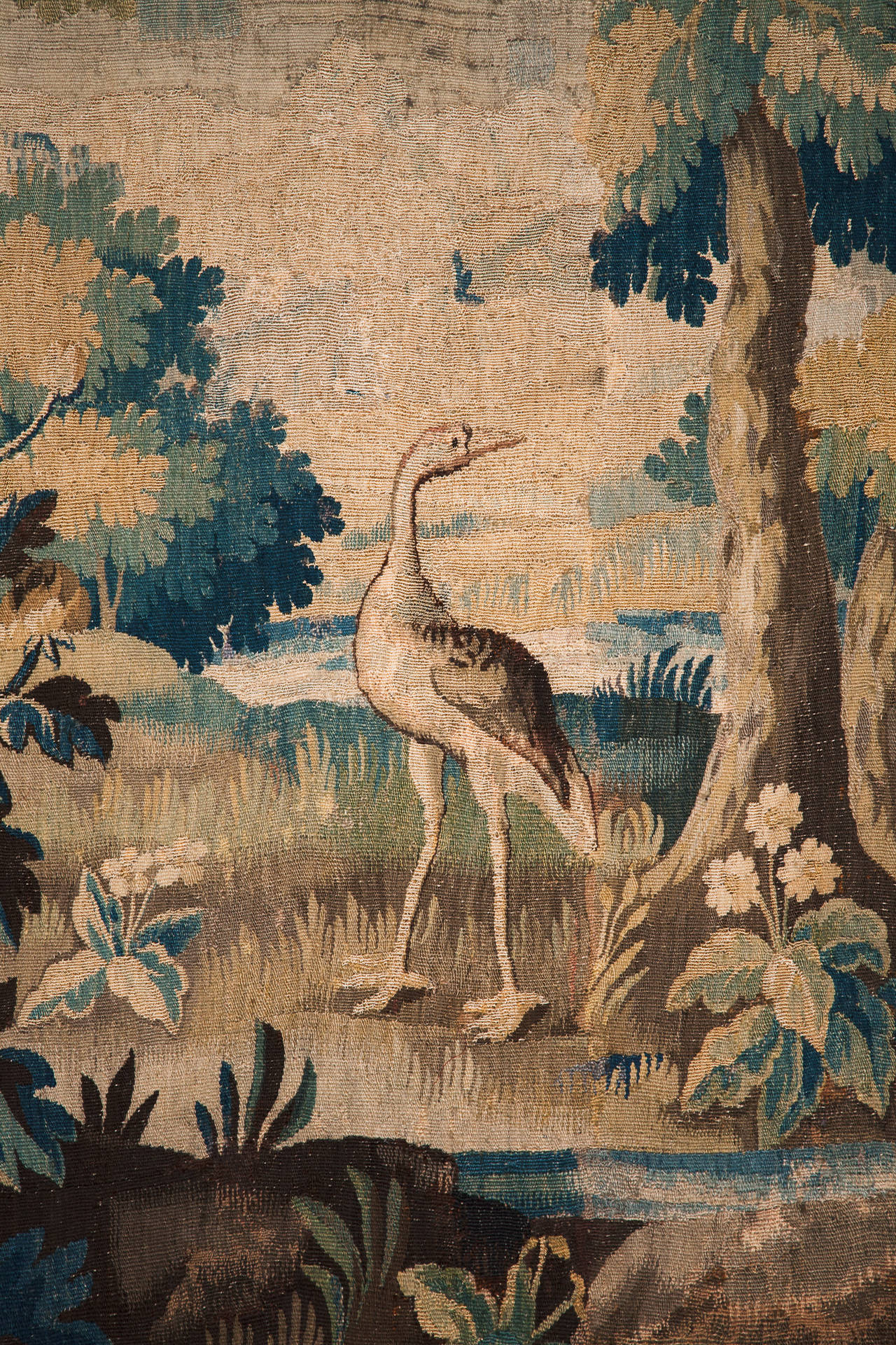 With two water birds wading in the foreground and a smaller bird resting on the branch of a tree. 
Surrounded by a border with flowers and ribbons. 
Woven in wool and silk. Backed with linen.