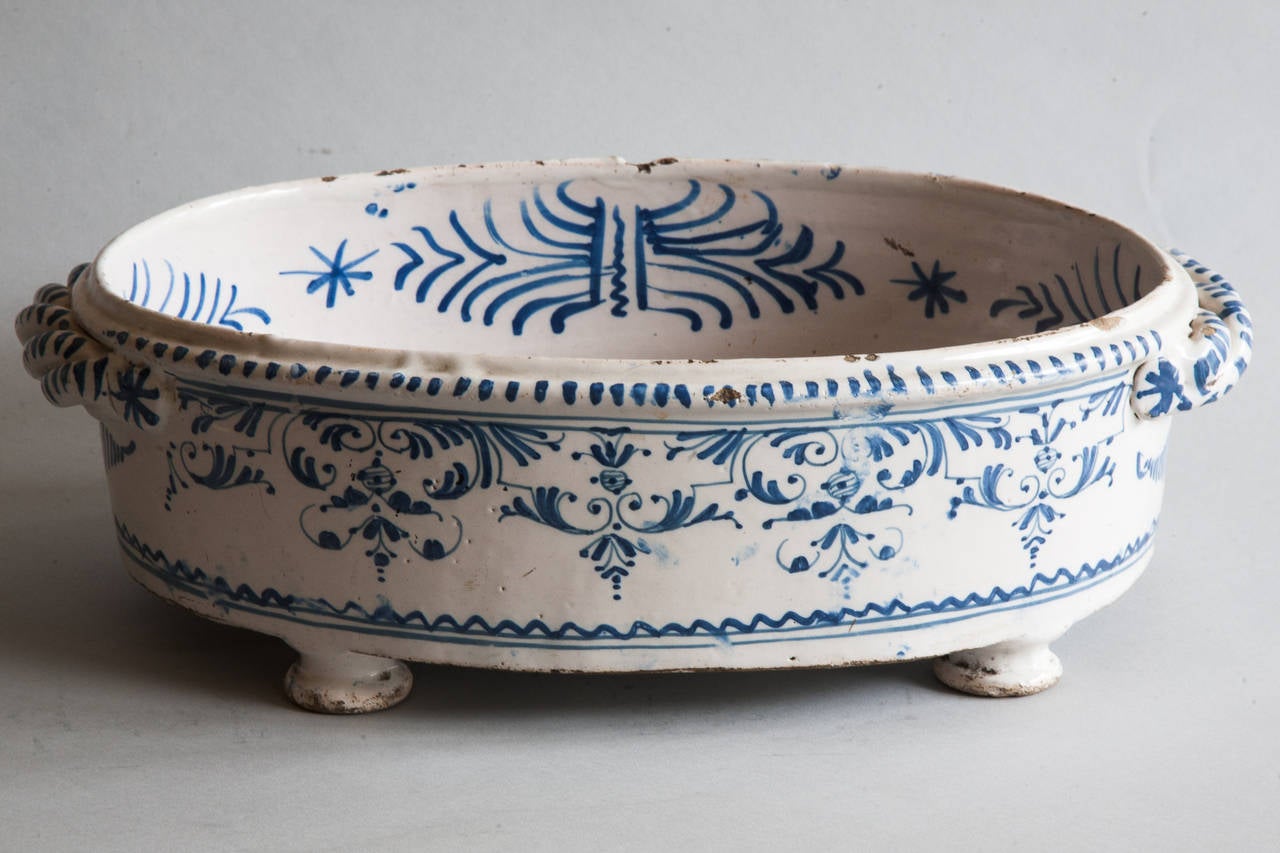 Tin-enameled earthenware decorated in camaïeu bleu a (monochrome) technique to decorate a fine milky-white background. 
Standing on three round bun feet decorated shades of blue on a milky white background with a central motif inside and decorated