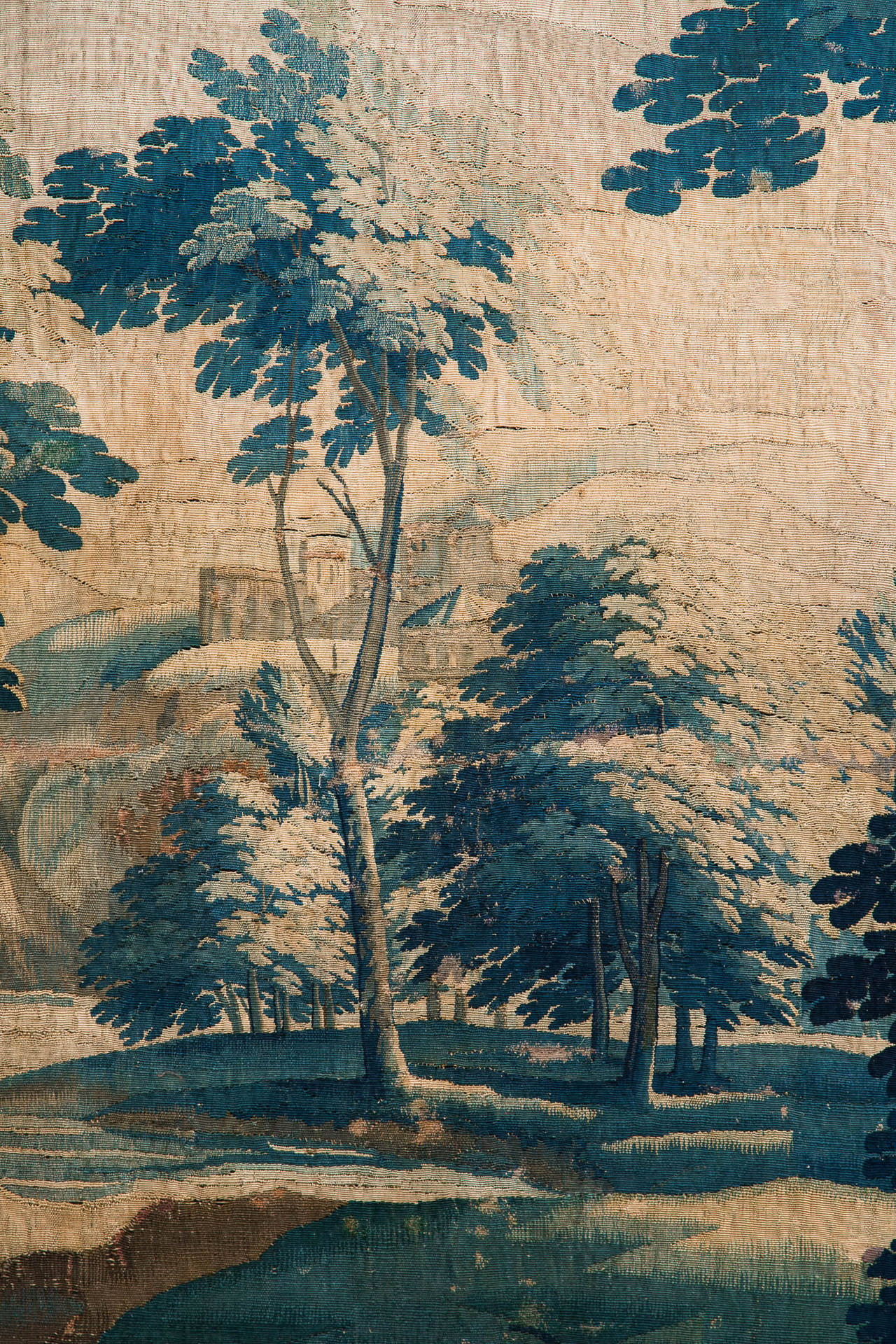 With trees and plants to the foreground and a chateau on a hill in the background with a waterfall and a river, surrounded by a floral border. Finely woven in wool and silk.