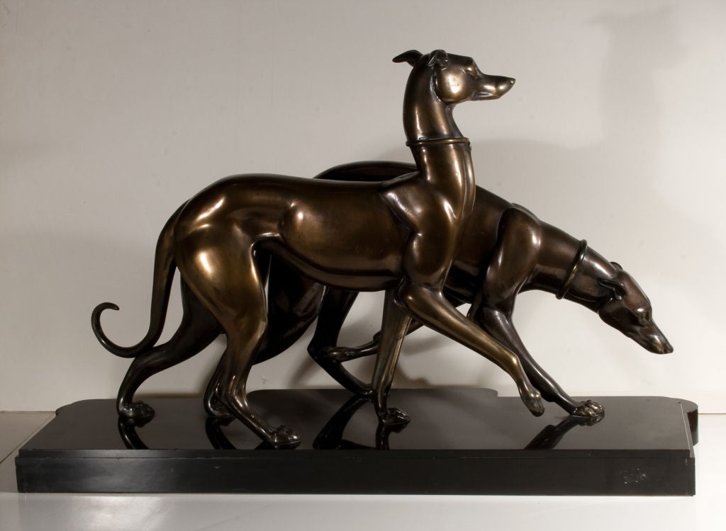 Paire de statues à grande échelle de whippets ou de lévriers italiens. Régule, ou speltre patiné dans une finition bronze, sur un socle en marbre noir et onyx beige veiné. Signé sur la base ROCHAS. Cette grande statue de chiens, typiquement déco,