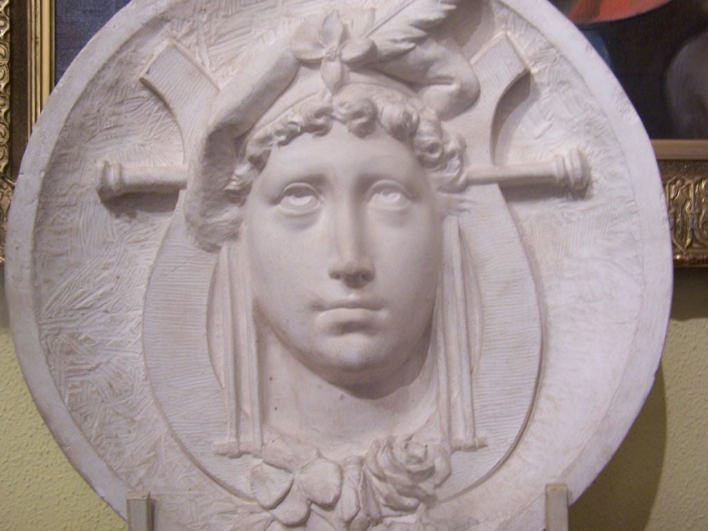A Large Plaster Roundel depicting an Allegorical Female Figure wearing liberty cap with a feather.  Also showing pole, rose, clover, and lyre.  Mounted on a wooden base. Base size: 21