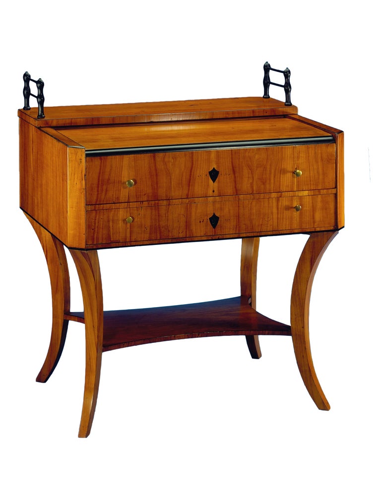 The two-drawer designed body with canted corners is topped by the bookends and raised on elegantly shaped Clismos legs with shelf. Veneered with cherry wood and bird's-eye maple on pine wood, ebonized trim, inlaid with ebony. Original hinges, brass