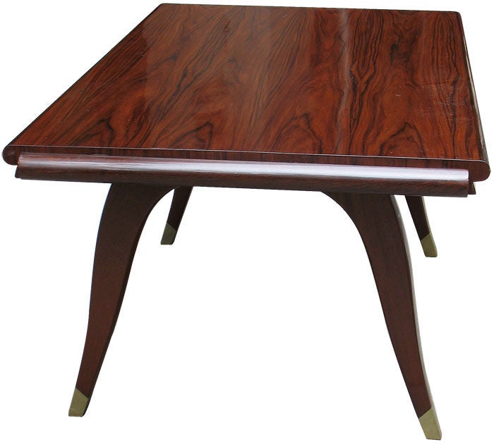A well proportioned and elegantly shaped French Art Deco dinning or conference table in rosewood. Matching veneered table top raised on two inverted U-form supports ending in original brass sabots. The table opens up with original pull-out ledgers