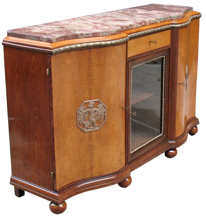 Serpentine front Art Deco buffet with three doors. One of them with glass panel and a drawer. Amboyna and mahogany. Four ball feet. Original marble top and patinated ribbon twist brass moldings, original locks, keys, escutcheons, hinges and brass