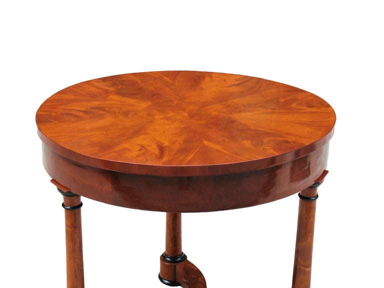 This small diameter Biedermeier table is matching veneered in rare tobacco colored mahogany on oak and pine. Ebonized trim. Outstanding architectural design with three conical Doric columns and a tripartite serpentine base.

References are