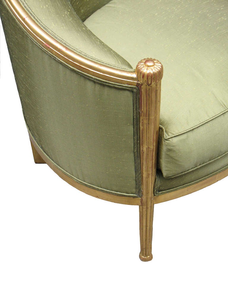 Pair of Paul Follot inspired French Art Deco barrel-back bergeres with gilt-wood frames (24 Karat) and fluted, tapered front posts topped with finely carved rosettes and ending in ball feet. Upholstered with platform and loose cushion seat.