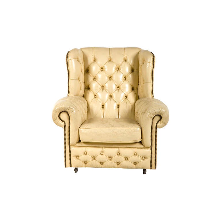Vintage tufted wingback chair. original creme leather upholstery. antique brass nailhead trim. Circa 1960. Set of two available (priced individually).