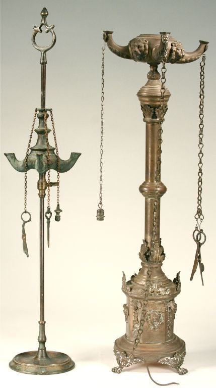 These authentic Victorian oil lamps will help light the way! Cast in brass, they're hung with the various accessories for use - wick cutters, snuffers, etc. The more ornate of the two is decorated with putti, lion's heads, and ram's heads, and it