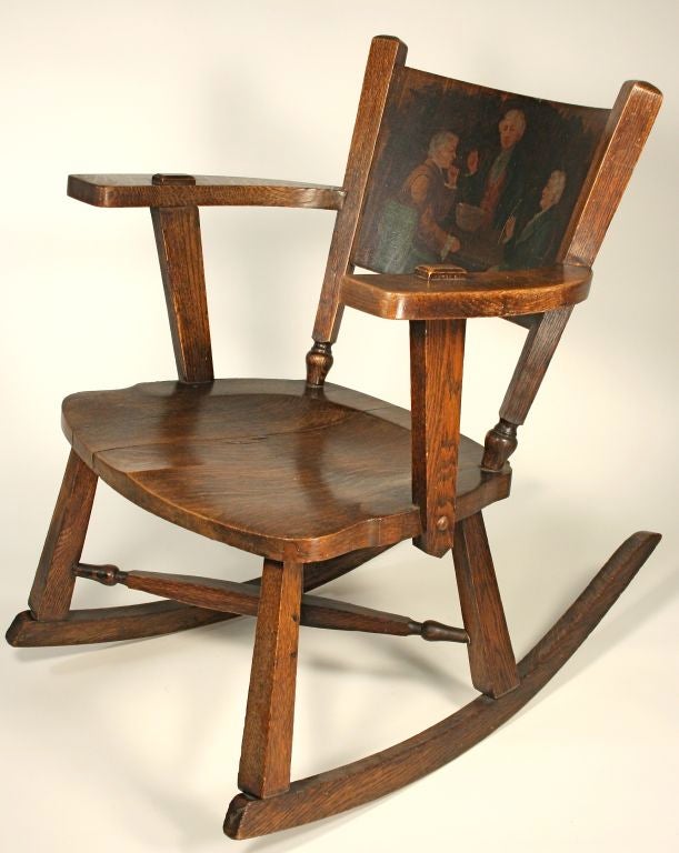 This charming and sturdy rocker, fashioned of English curly oak, features x-stretchers, and through mortise & tenons on the arms -- a common feature of Arts and Crafts joinery. The painting on the back shows a group of three gentlemen around a