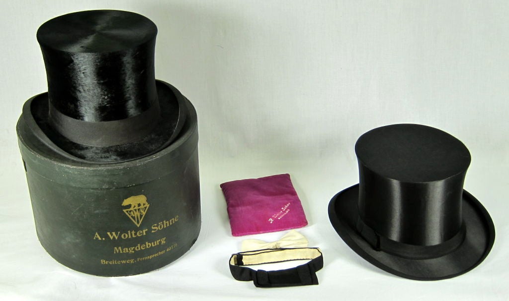 Description: Original box Wolter Shohne  Magdeburg Germany hat box. One beaver felt top hat. 1 silk retractable Gibus top hoat<br />
1- white bow tie, 1 black bow tie Velvet magenta polishing cloth.<br />
<br />
Measurements: <br />
Box:
