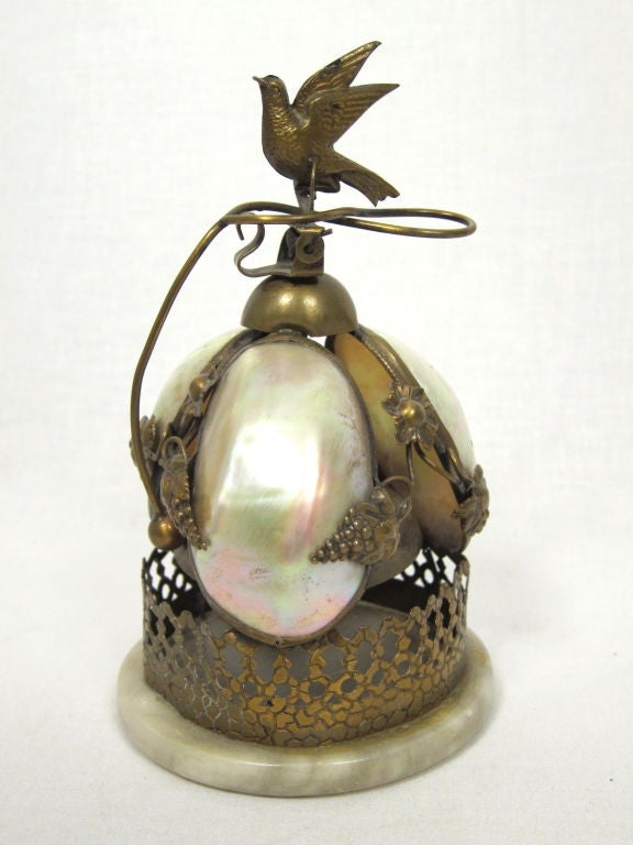 Featured is a lovely example of Art Nouveau craftsmanship in this swallow-topped bell from the late Victorian period. Set atop a veined marble base, the pierced brass supports 3 rainbow-hued mother of pearl leaves interspersed with grape and floral