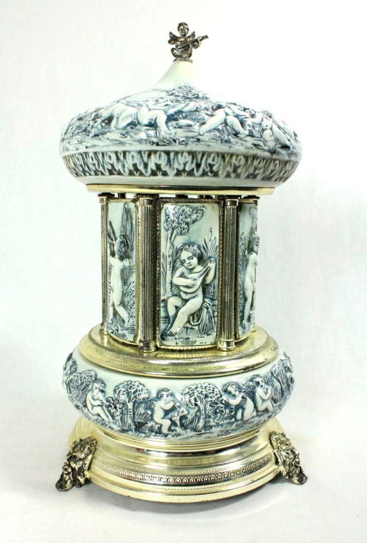 VINTAGE ITALIAN PORCELAIN CHERUB MUSIC BOX CAROUSEL. This beautiful piece features playful cherubs in various scenes with a winged cherub playing mandolin on top. The doors swing open and music plays upon triggering a small button on the side. A