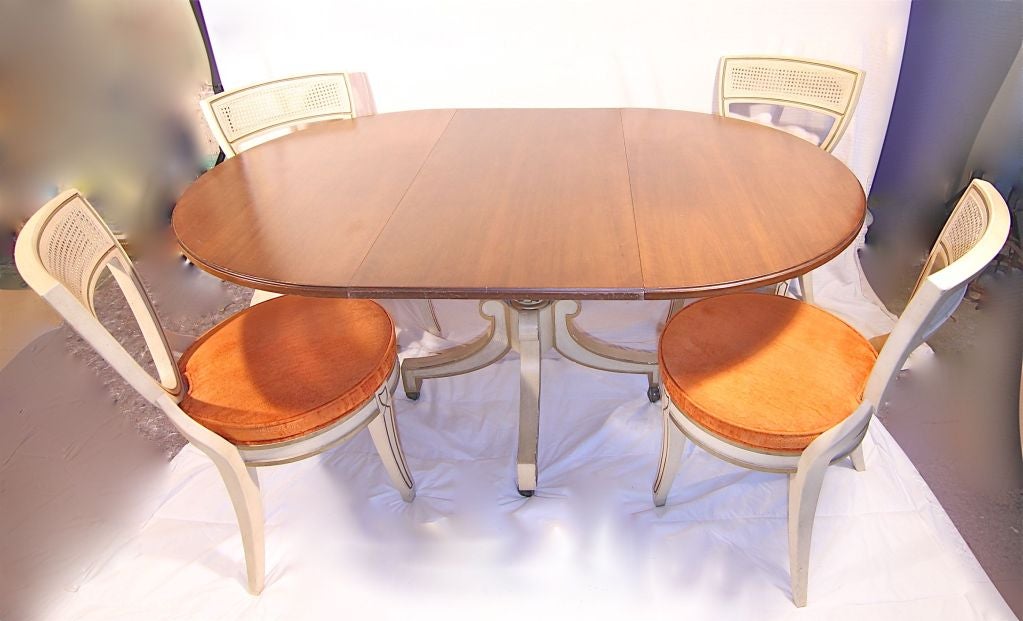 Dorothy Draper dining table. Walnut table top with pedestal of gold and cream color on wheels. The table has an extension. The chairs are caned with same gold and cream color orange upholstery. <br />
Chairs: <br />
Seat height: 17